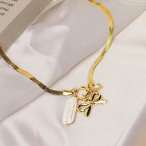 Sophisticated gold necklace featuring bow and pearl charms on silky fabric background.