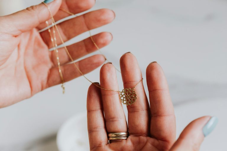 Close-up of a delicate gold necklace being held between hands, featuring an intricate pendant design.